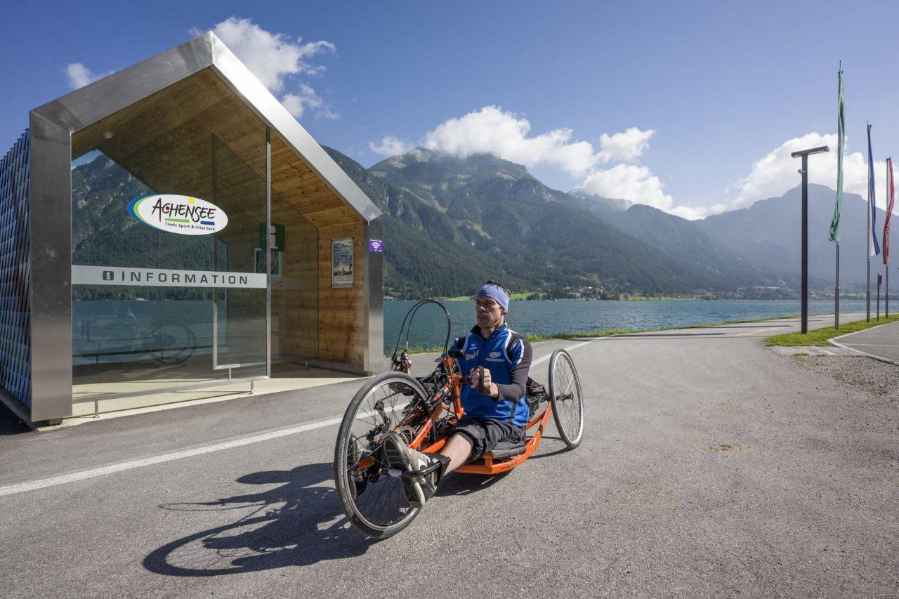 Mann im Handbike am Achensee mit Informationsgebäude.