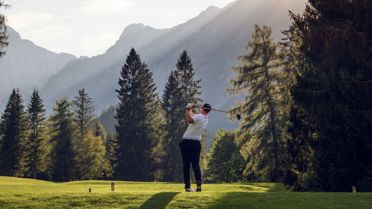 Golfer bei der Schwungausführung im Gebirge.