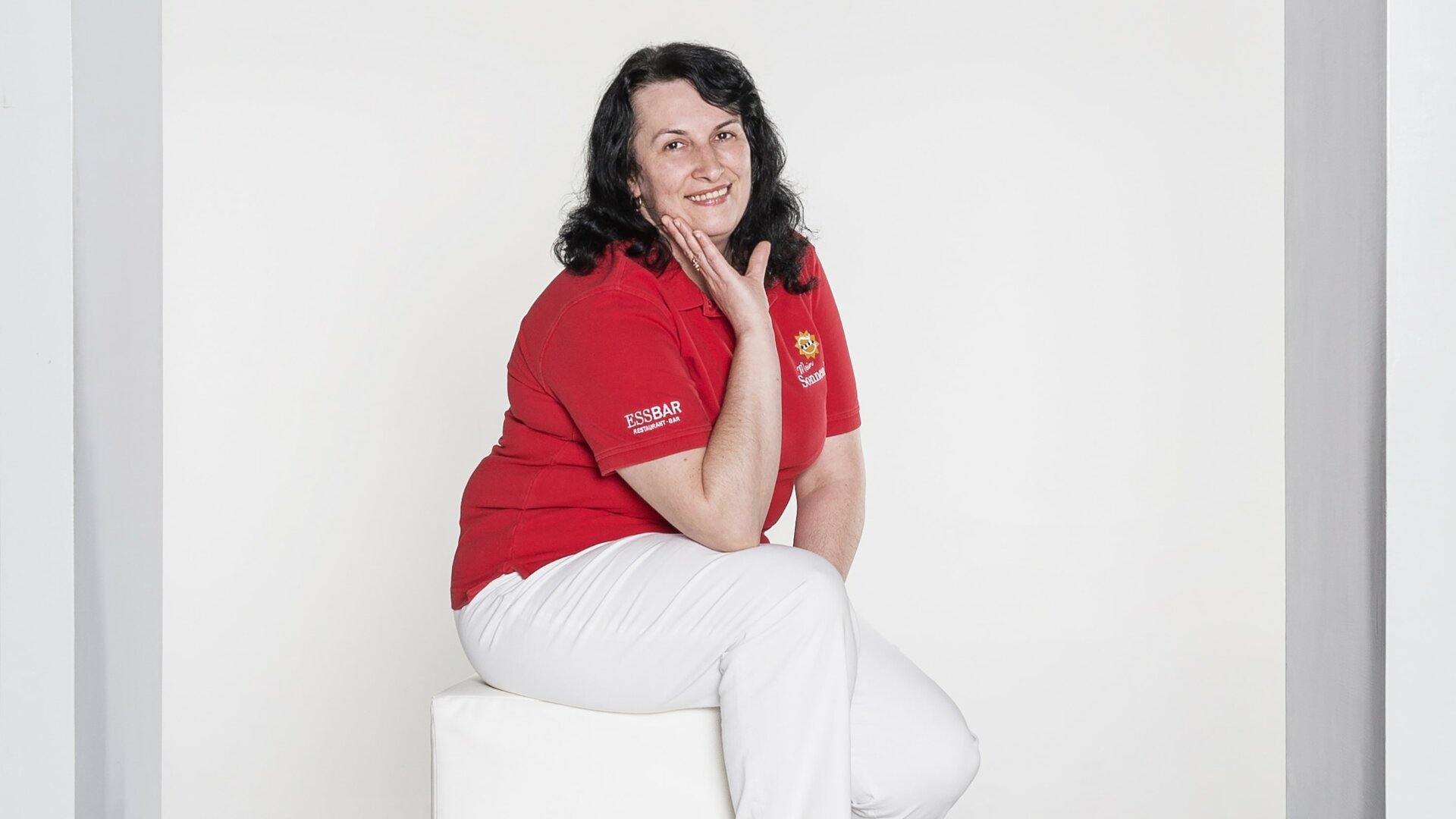 Lächelnde Frau in roter Bluse auf Sitzblock.