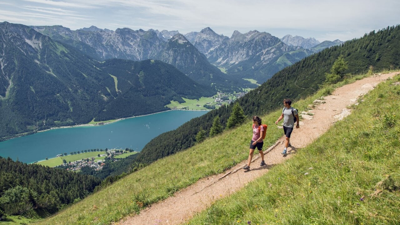 Zwei Wanderer auf einem Bergweg mit See.