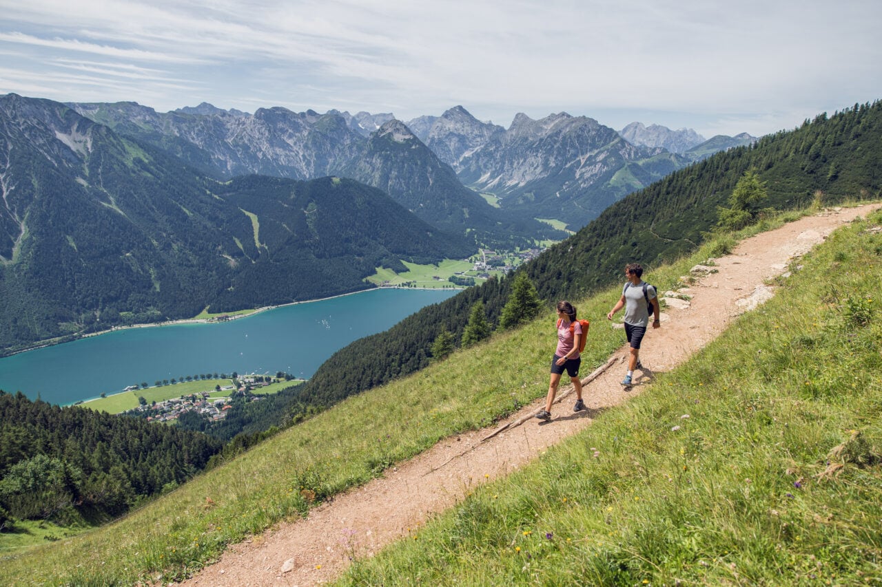 Zwei Wanderer auf einem Bergweg mit See.