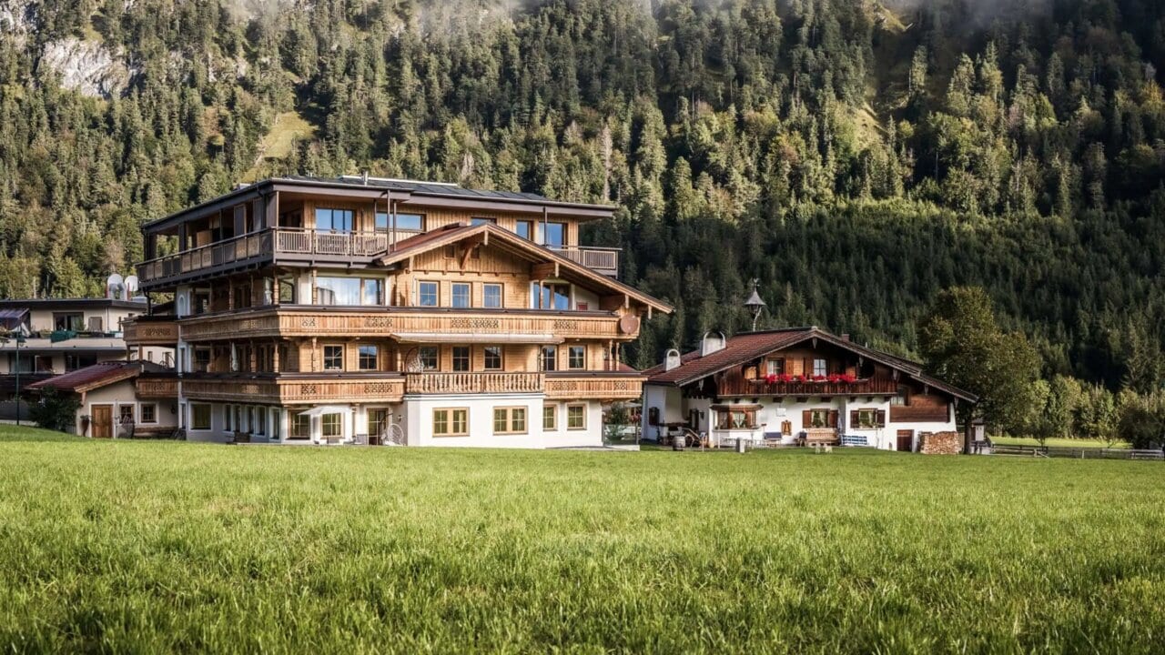 Alpenhaus auf grüner Wiese vor Waldkulisse.