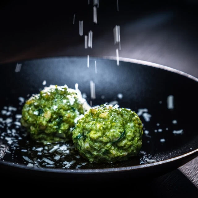Grüne Bällchen mit Salz in schwarzem Teller.